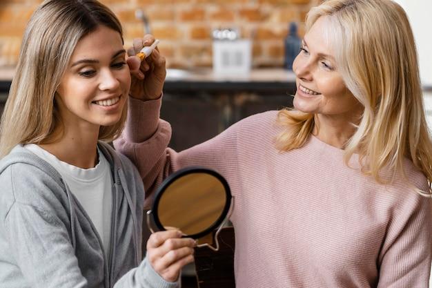 Mother helping young woman apply makeup at home