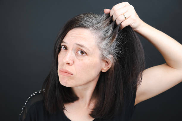 Woman examining her gray hair with a confused expression on a dark background