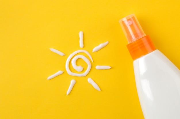 Sunscreen spray bottle on a yellow background with a sun symbol made of sunscreen cream.