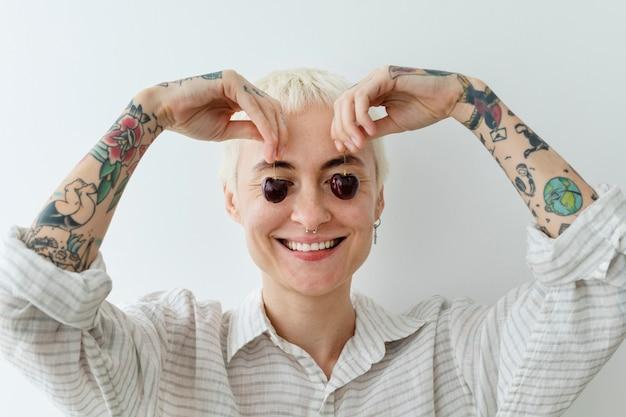 Woman with short blond hair and tattoos forming heart shape with hands over eyes